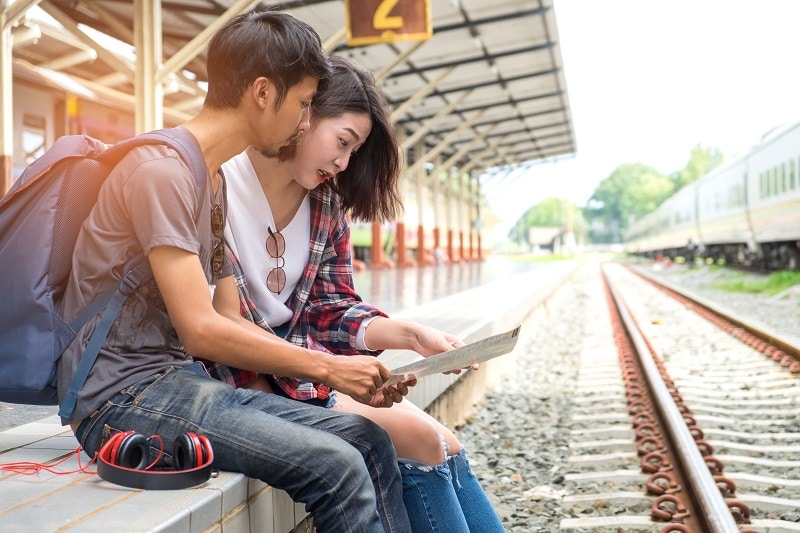 Asian male and female tourists planning a train trip.