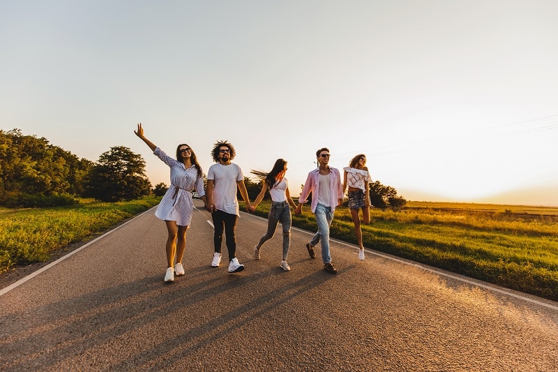 Company of happy young stylish guys walk on a country road on a sunny day