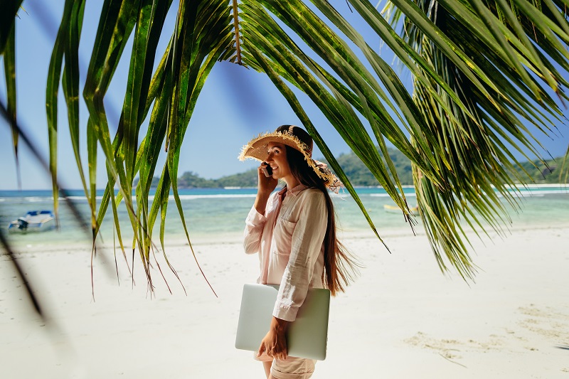 Woman talking on phone with laptop on beach