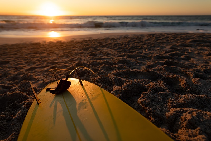 Surfboard lying on a sandy beach with calm sea and a clear sky at sunset
