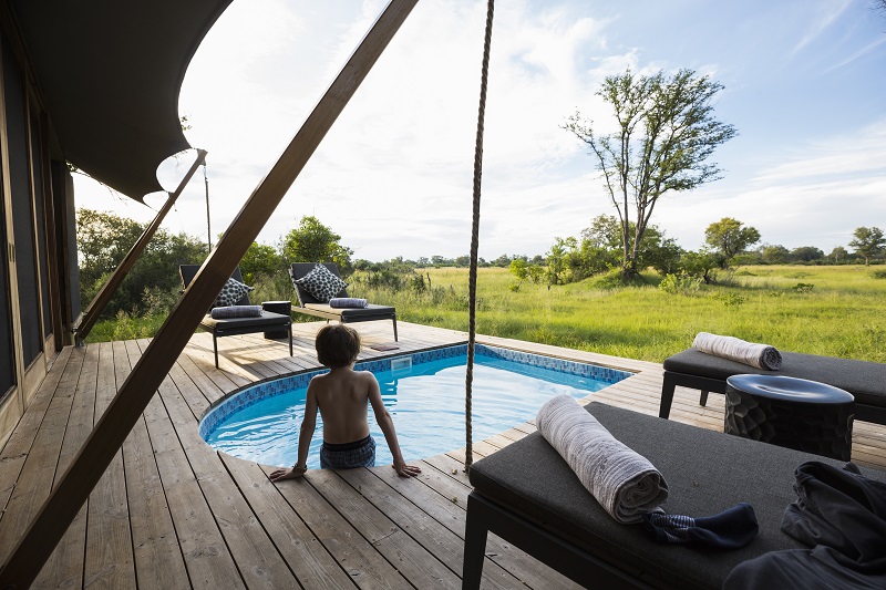 Botswana,A boy in a swimming pool at a safari camp, looking out over the landscape