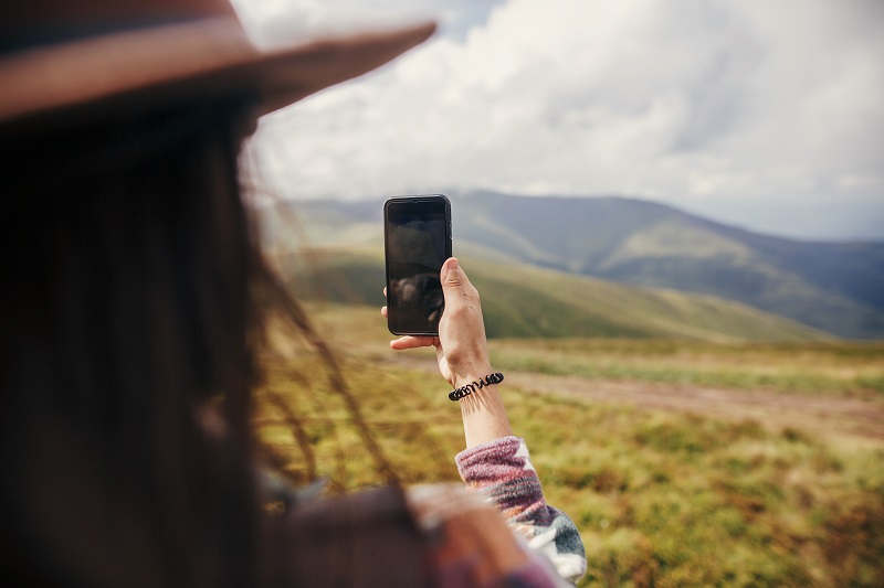 stylish traveler girl in hat with windy hair holding phone on to