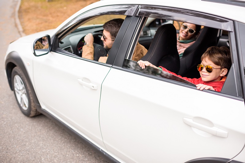 Happy friendly family travelling by car on rural road