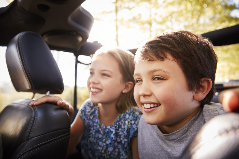 Children Sitting In Back Seat Of Open Top Car On Road Trip