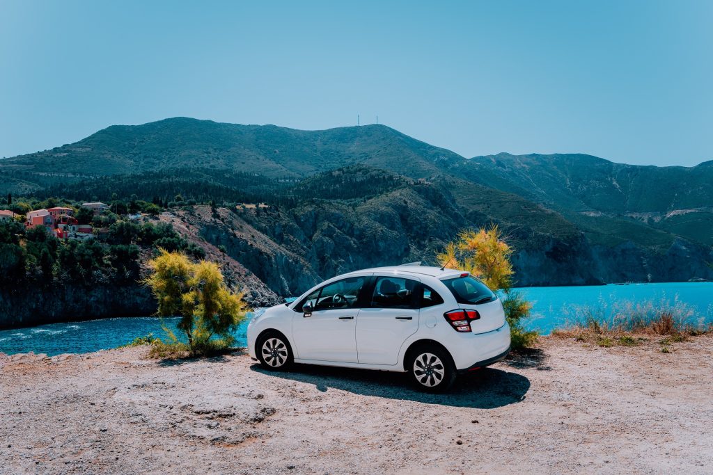 Vacation travel with car concept. Rental hired car in front of amazing bay with turquoise water. Discover Mediterranean Islands. Summer time holiday trip