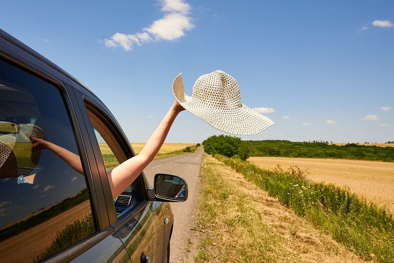 Female hand holding their hat out the car window during a road trip.