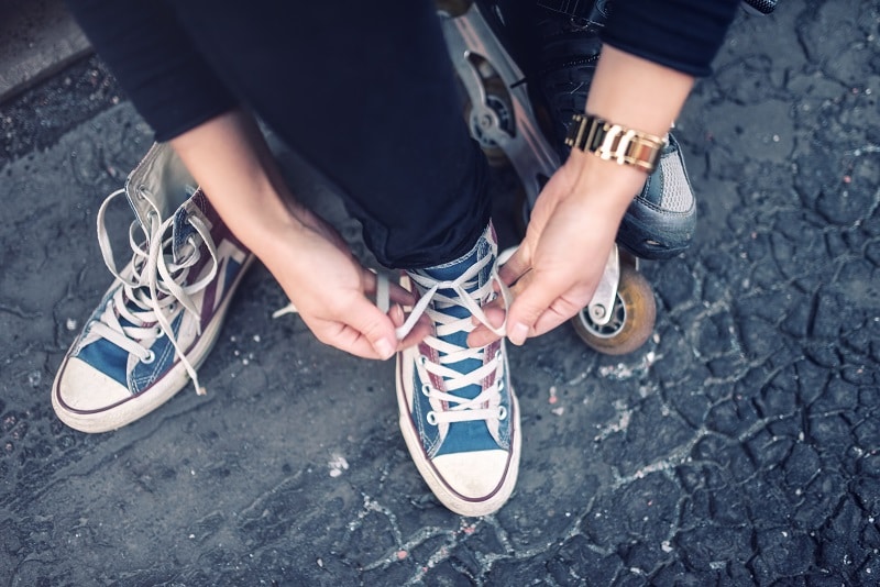 Hipster wearing sneakers, teenager tieing laces at sport shoes. Urban lifestyle with footwear and modern clothing.