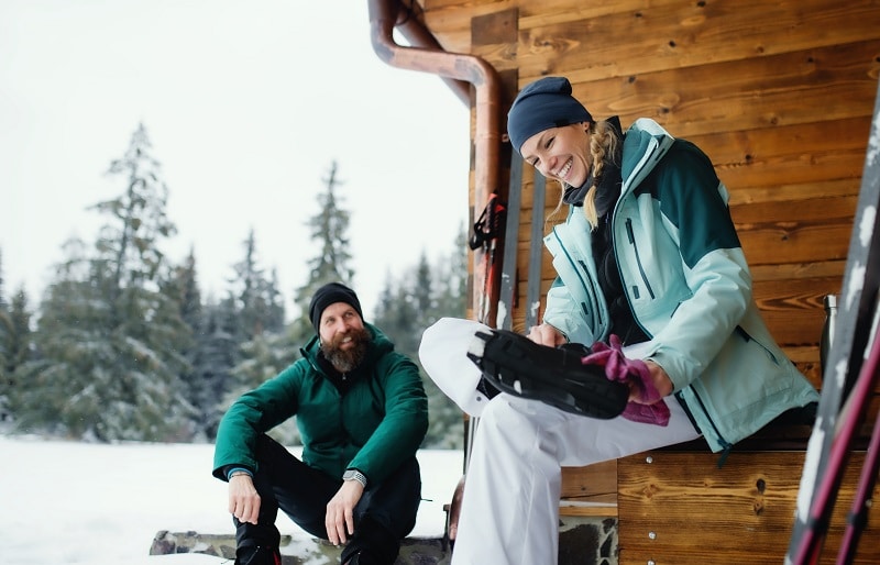 Mature couple resting by wooden hut outdoors in winter nature, cross country skiing.