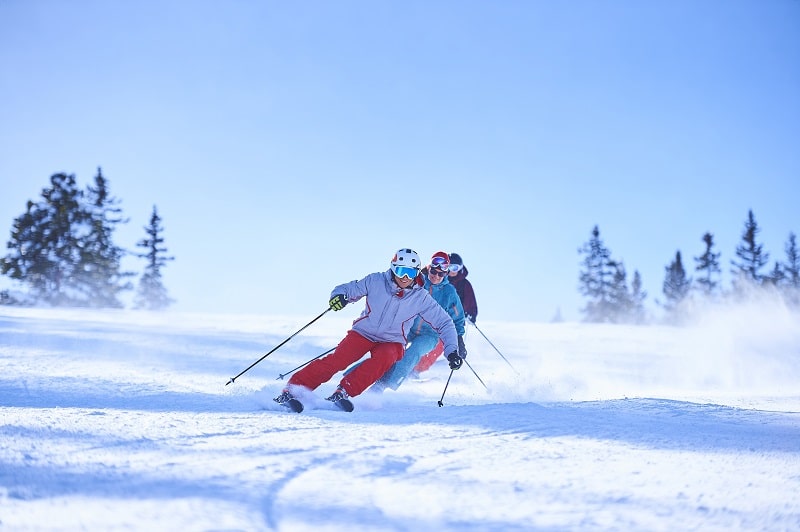 row-of-male-and-female-skiers-skiing-down-snow-covered