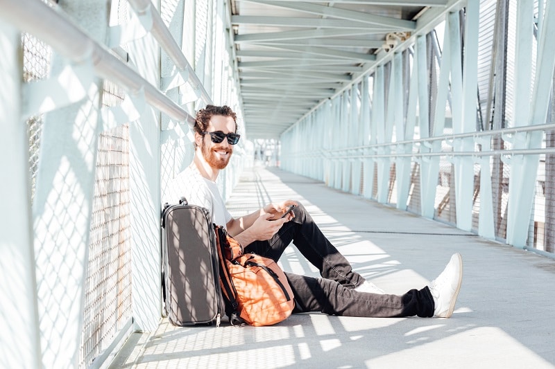 Urban young man talking on smart phone traveling inside in airport. Casual young businessman wearing suit jacket. Handsome male model. Young man with cellphone at the airport while waiting for