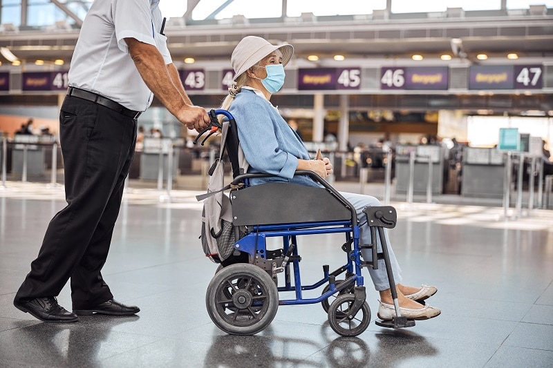 Airline worker rolling a wheelchair with a disabled woman