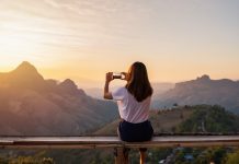 Young woman traveler taking photo with smart phone at sunset over the mountain