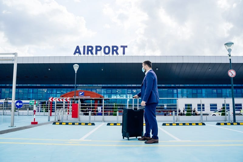 side view of a man in suit with mask on face waiting near the airport.