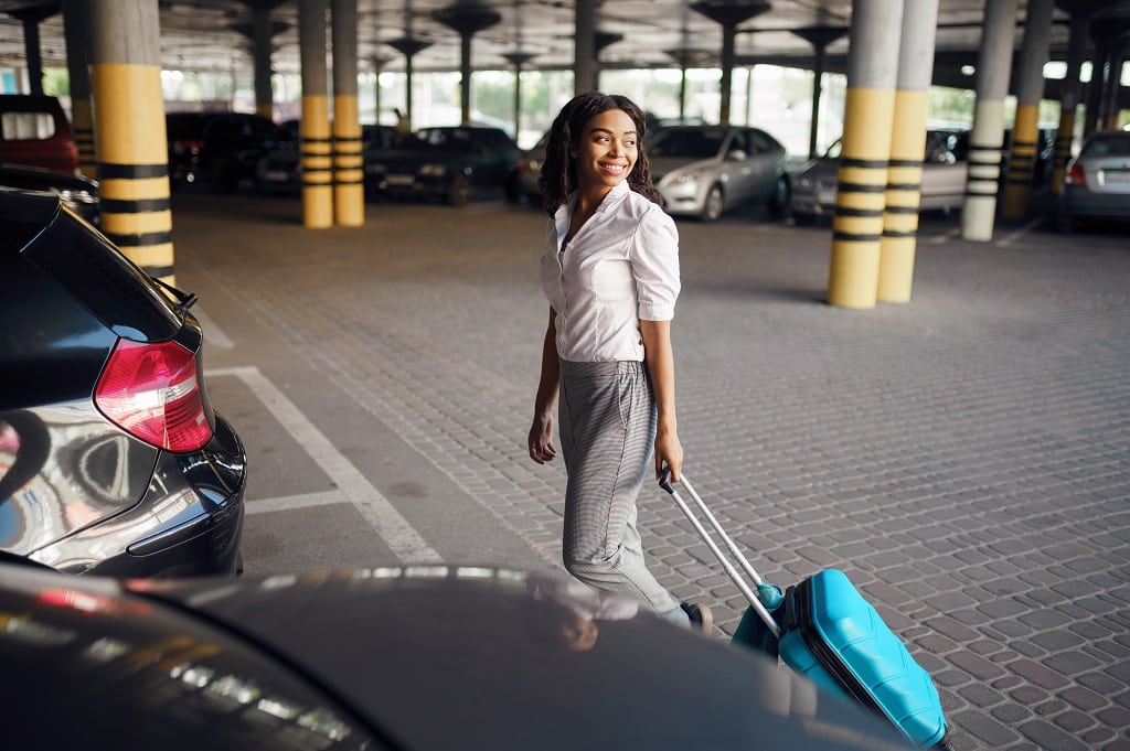 Young woman with suitcase in car parking