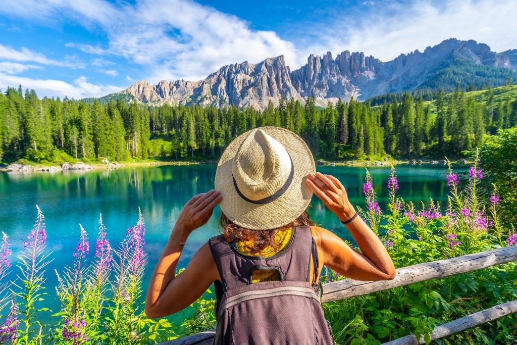 Tourist holding her hat enjoying the breathtaking view of lake carezza and latemar mountain in the italian dolomites